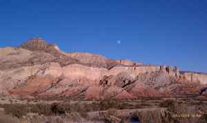 An almost full moon rises in the mountain distance.