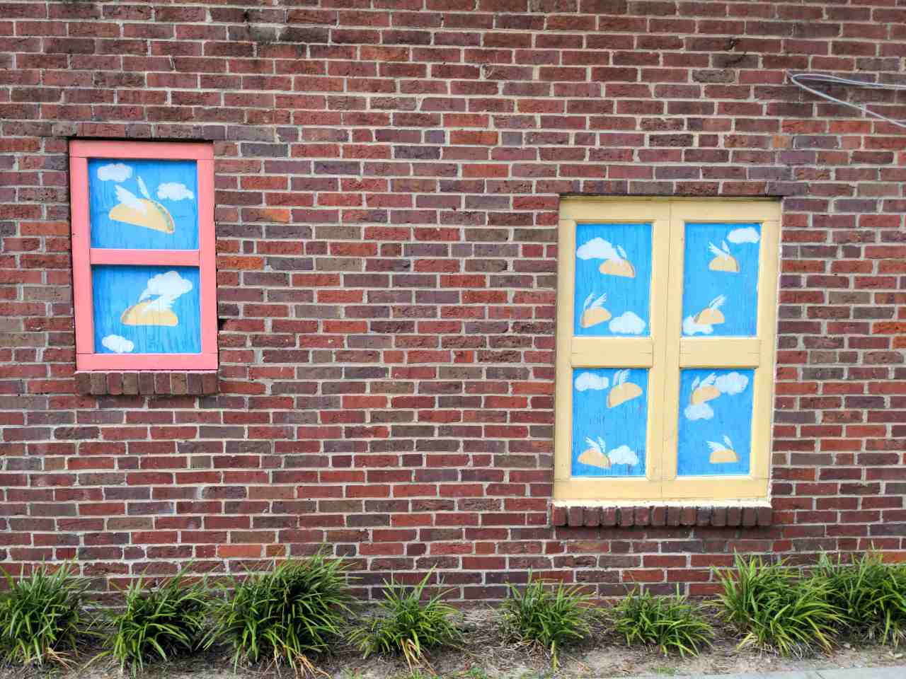 Murals on brick wall. They look like windows and through them you see flying tacos.