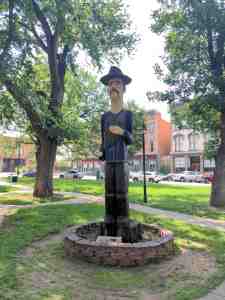 Wood sculpture of a farm worker stands in a town plaza.