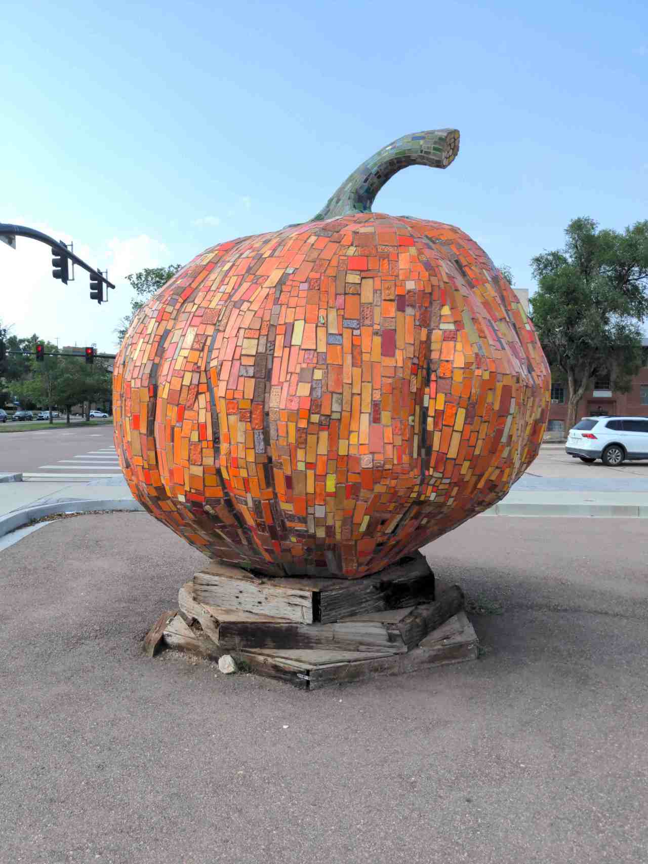Mosaic sculpture of a giant pumpkin made with lots of orange tiles. Green tiles make the stem.