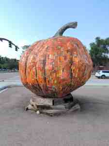 Mosaic sculpture of a giant pumpkin made with lots of orange tiles. Green tiles make the stem.