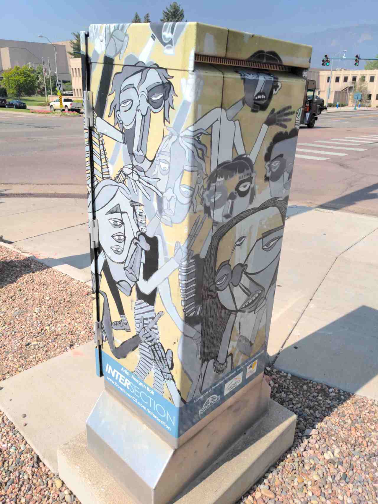 Mini mural of abstract people on utility box on street corner.