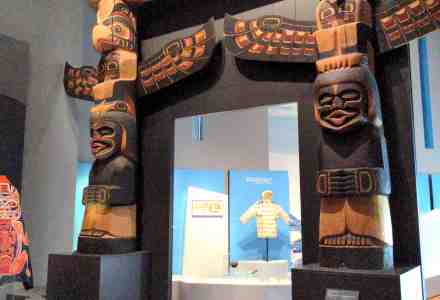 Portal between art exhibits is bordered and crowned by tall wood carved totem poles.