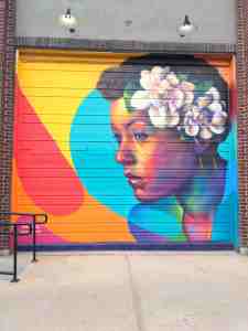 A woman's head and shoulders, flowers in hair, against a backdrop of vibrant colors.