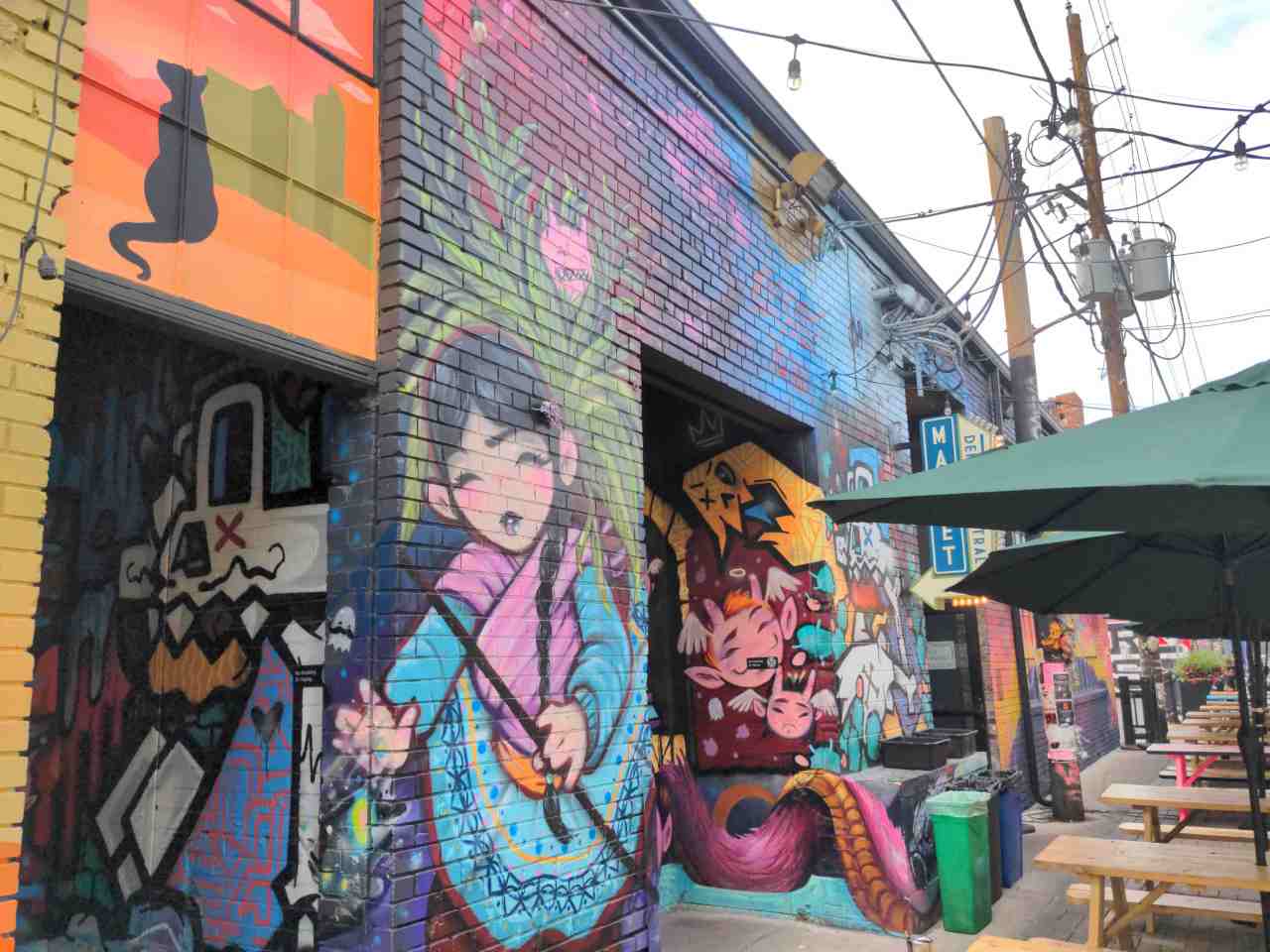 A wall painted mural full of cartoonish and anime type characters.