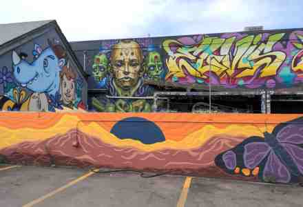 Multiple building wall murals full of color and weird cartoonish characters.