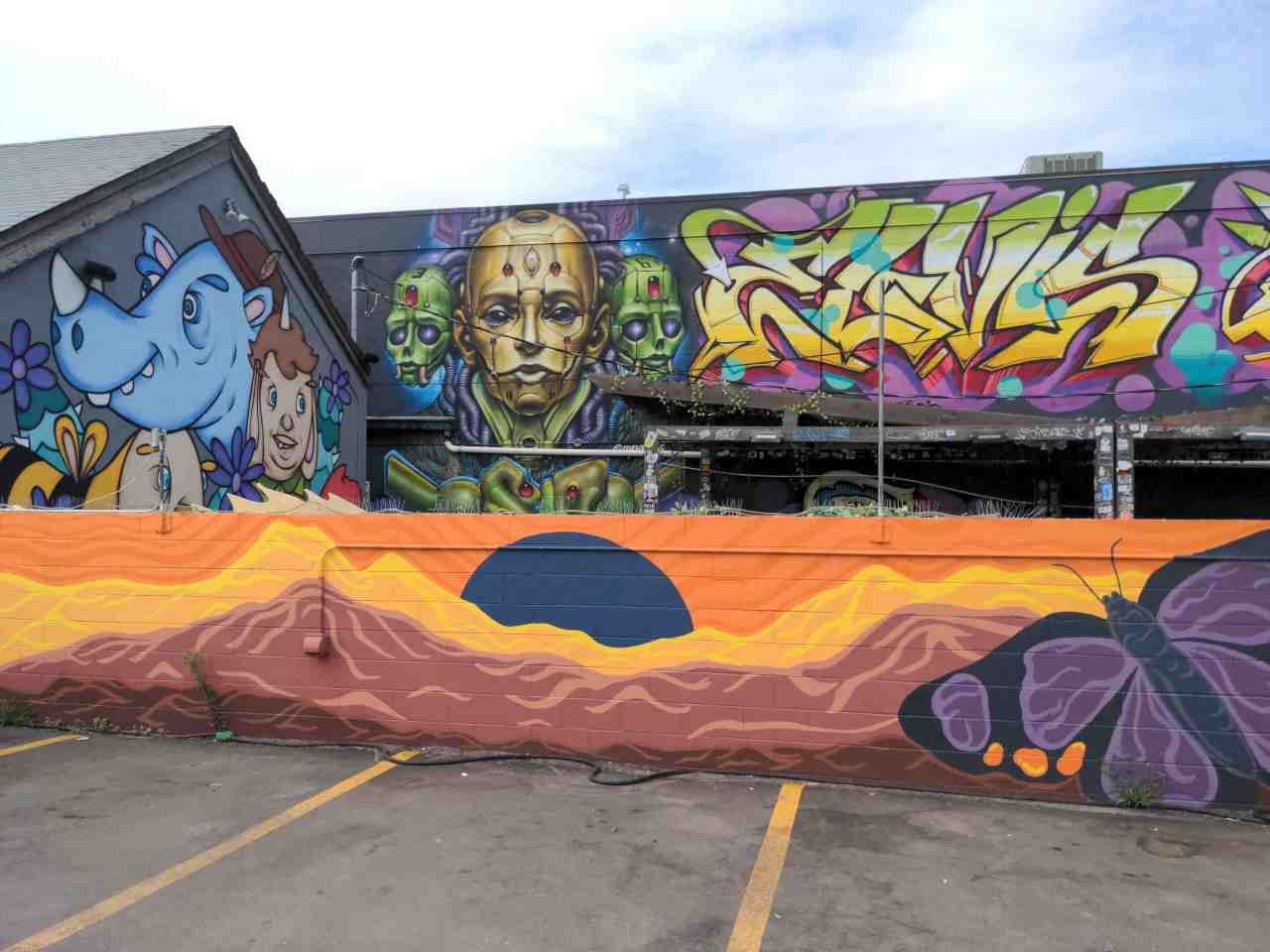 Multiple building wall murals full of color and weird cartoonish characters.