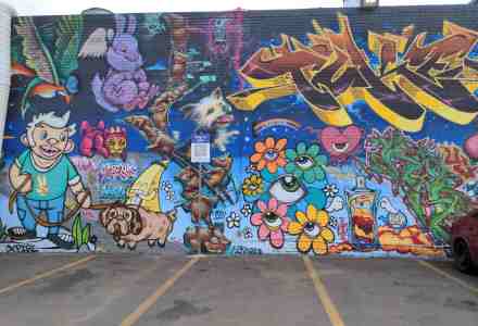 Building wall mural full of colorful graffiti and goofy looking cartoonish characters and creatures.