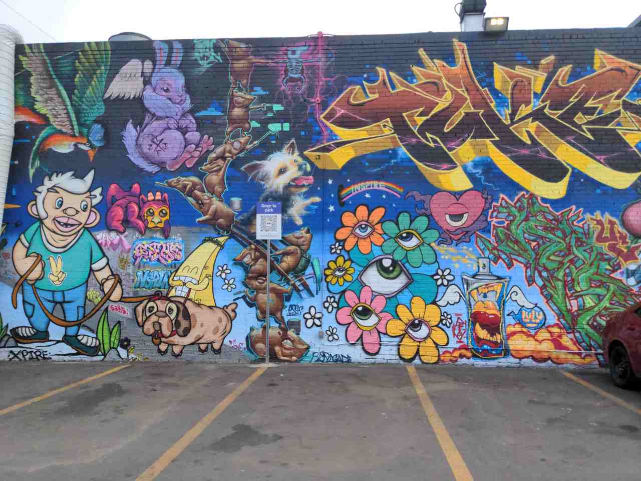 Building wall mural full of colorful graffiti and goofy looking cartoonish characters and creatures.